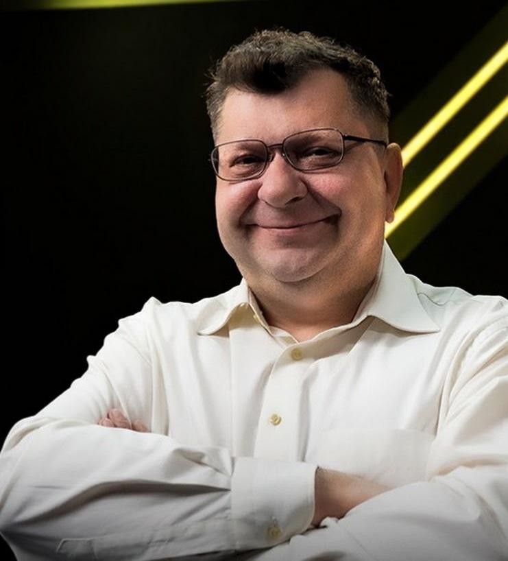 Zbigniew Stonoga podczas nagrywania wideobloga lub sesji w mediach społecznościowych, patrzący prosto w kamerę z ekspresyjnym wyrazem twarzy, na tle nowoczesnego wnętrza z subtelnymi elementami technologicznymi, oświetlony naturalnym światłem, co podkreśla jego autentyczność i bezpośrednią komunikację z odbiorcami.