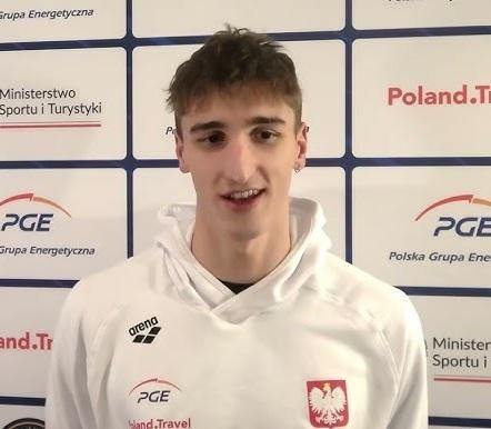 Ksawery Masiuk, polski pływak, stojący zamyślony przy basenie, symbolizujący połączenie kariery sportowej i edukacji w Teksasie.