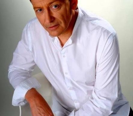 Jacek Borkowski na scenie teatralnej, w środku występu lub podczas ukłonu, w teatralnym stroju, z widocznym oświetleniem scenicznym.