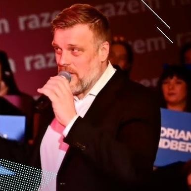 Alt: Adrian Zandberg podczas wystąpienia publicznego, z pasją przemawiający do zgromadzonych, symbolizujący jego zaangażowanie w kampanię polityczną.