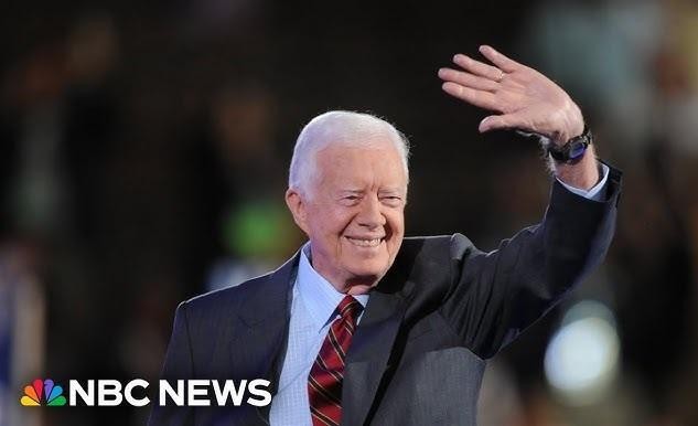Jimmy Carter w roboczym ubraniu i kasku, aktywnie uczestniczący w budowie domu dla Habitat for Humanity, symbolizujący jego zaangażowanie w działalność humanitarną.