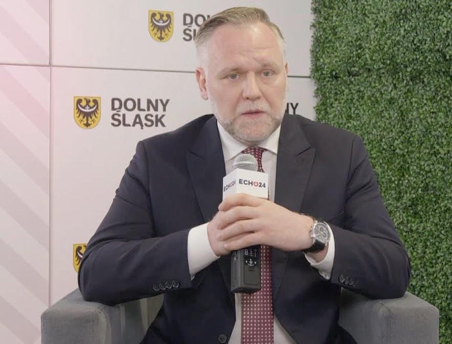 Dawid Jackiewicz, polityk, w dynamicznej pozie, na rozmytym tle symbolizującym rozwój gospodarczy i energetyczny, np. turbiny wiatrowe lub wykresy.