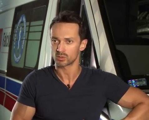Rafał Cieszyński na planie telewizyjnym, uśmiechnięty i charyzmatyczny, w otoczeniu subtelnych elementów scenografii.