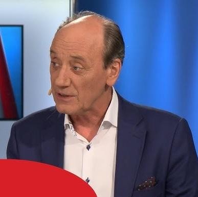 Dariusz Szpakowski komentujący mecz piłkarski w studiu, z widokiem na stadion w tle.