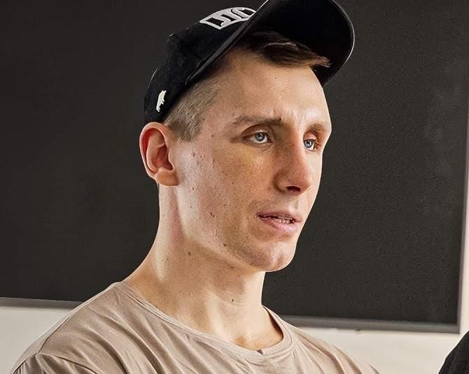 Alt: Michał Owczarzak (Owca WK) w dynamicznej pozie na siłowni, prezentujący imponującą muskulaturę podczas ćwiczeń siłowych, z widocznym sprzętem do treningu.