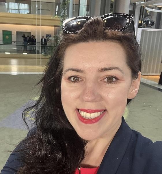 Dominika Ćosić w dynamicznej pozie, prawdopodobnie podczas wystąpienia lub pracy w środowisku medialnym, ukazująca jej zaangażowanie w dziennikarstwo międzynarodowe.