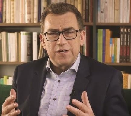 Maciej Orłoś w ujęciu filmowym, nawiązującym do jego ról aktorskich, z naciskiem na ekspresję i artystyczne oświetlenie.