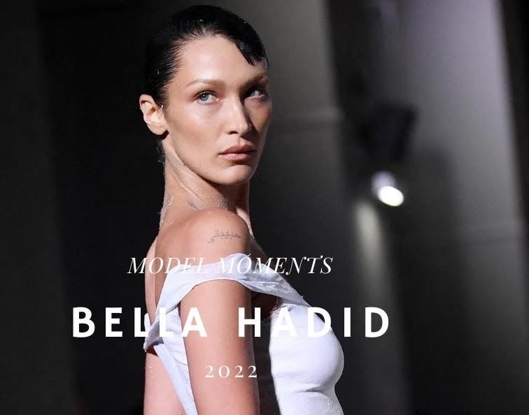 Bella Hadid na wydarzeniu modowym, w naturalnej pozie, z elementami luksusowego otoczenia w tle.